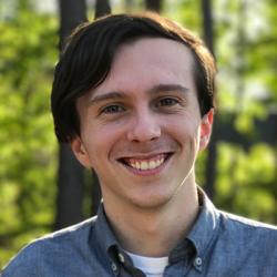 David Knudsen headshot, man smiling, standing in front of trees wearing a blue button up shirt