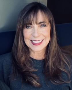 Denise Rael-Comstok headshot - Woman with straight brown hair and bangs smiles