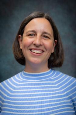 Headshot of woman from shoulders up, she has short brown hair, a blue and white striped shirt, and is smiling