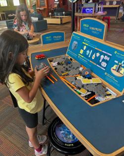 Children stand at opposite sides of the Design Build Test exhibit table, putting together the assorted pieces and testing their creations.