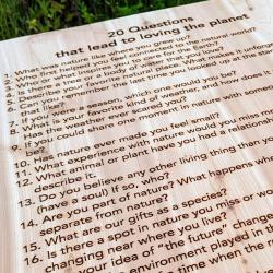A wood tabletop with engraved with the words across the top reads "20 Questions that lead to loving the planet."