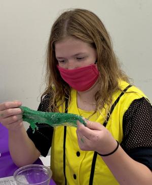 A girl with a red mask examines green slime in her hand. 