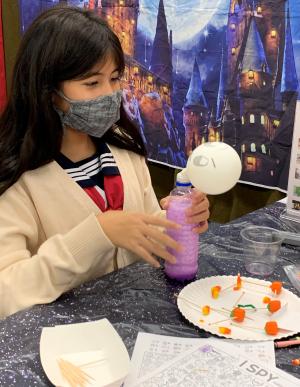 A girl creates a chemical reaction in a plastic bottle to make a white balloon, that looks like a ghost, expand. 