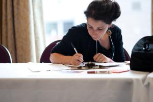 Person filling out a form on a clipboard at a table