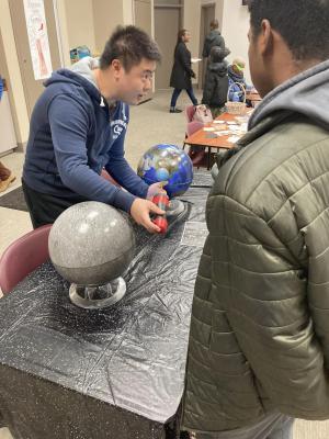 Facilitator stands at a table and shows models of the Earth and Moon to an adult learner.
