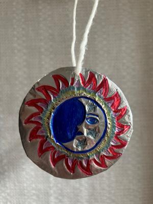 A colorful etching of the sun in tin foil with a string laced through the top in a loop.