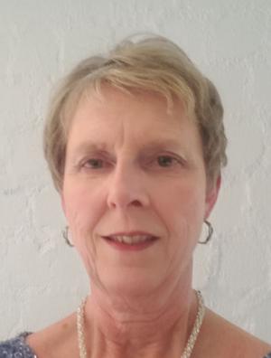 Headshot of an individual wearing pearls and hoop earrings. They have short light colored hair and they are smiling.