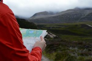 Navigating person holding a map looking at mountain clouds
