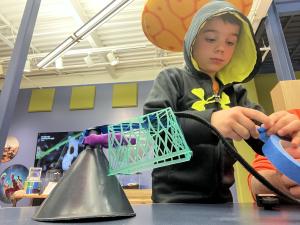 A child stands at a table focused on creating a contraption with random items and tape.