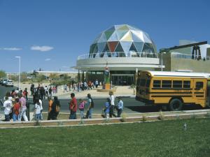 The front of the Explora Museum building, showing the large dome on top the entrance as a school bus drops a group of youth at the door.