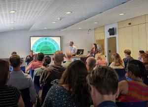 A large group watches a presentation, the current slide is a Decarbonization Infographic