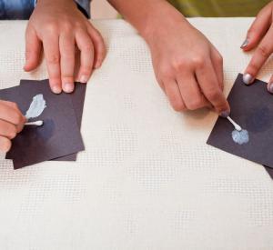 Hands using cotton swabs spreading sunblock on black paper using DIY Nano sunblock activity