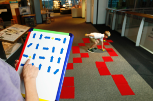 A learner gives commands to another learner who is blindfolded and is navigating a obstacle course.