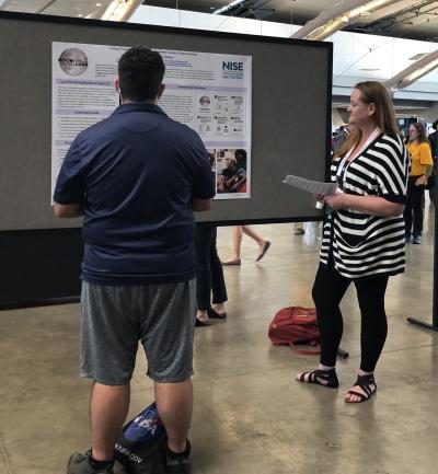Two informal science educators having a discussion about Moon Adventure Game poster during ASTC 2022 conference