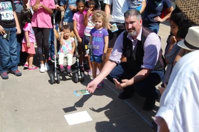 Facilitator kneels at center of crowd with a pinhole projector showing audiences the shadow of the 2023 Annular Solar Eclipse.