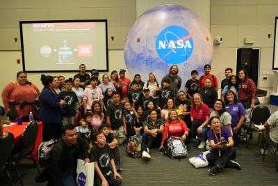 Staff and Participants Pose for a Group Shot Inside in Front of an Inflatable Glove with the NASA Logo