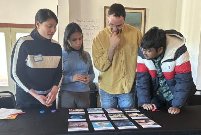 Crowd stands around a table where the Neuro Futures Card Game is Spread Across for Discussion