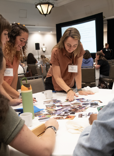 Individuals stand around a table that has colorful cards scattered across.