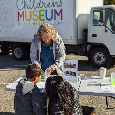 Facilitator using the Voyage through the Solar System Breath of Fresh Air activity at a table setup outside as two young participants are engaged.