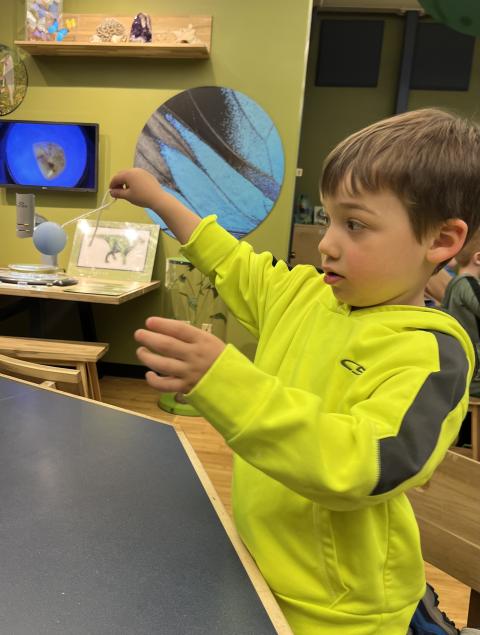 A child in a bright yellow sweatshirt spins a ball on a string while watching intently.