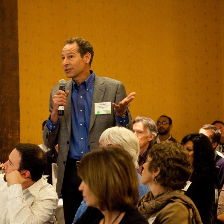 Man standing with microphone in a group forum discussing STEM topics societal implications