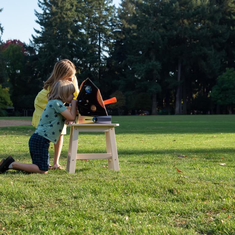 Two learners observe the Sun with a solarscope in a grassy field