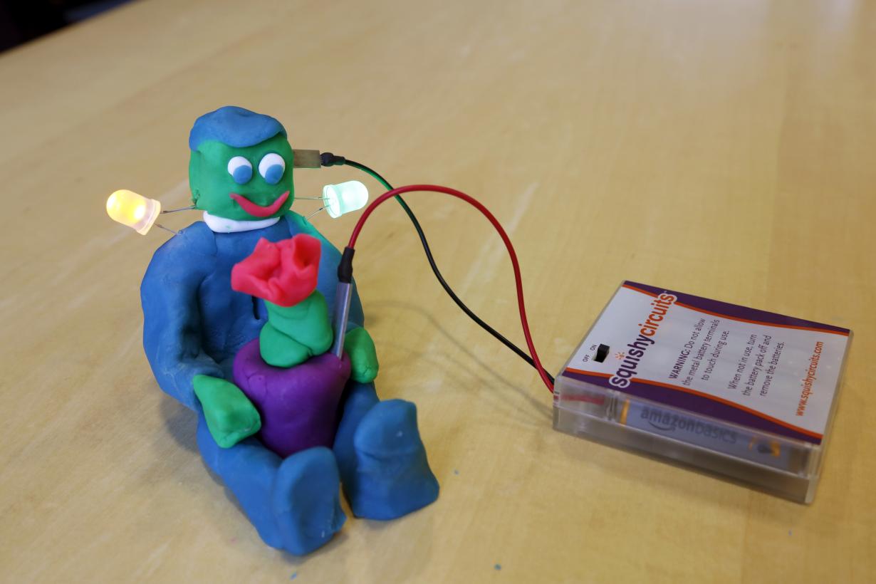 Lit up dough creature holding flower with squishy circuit battery pack and wires