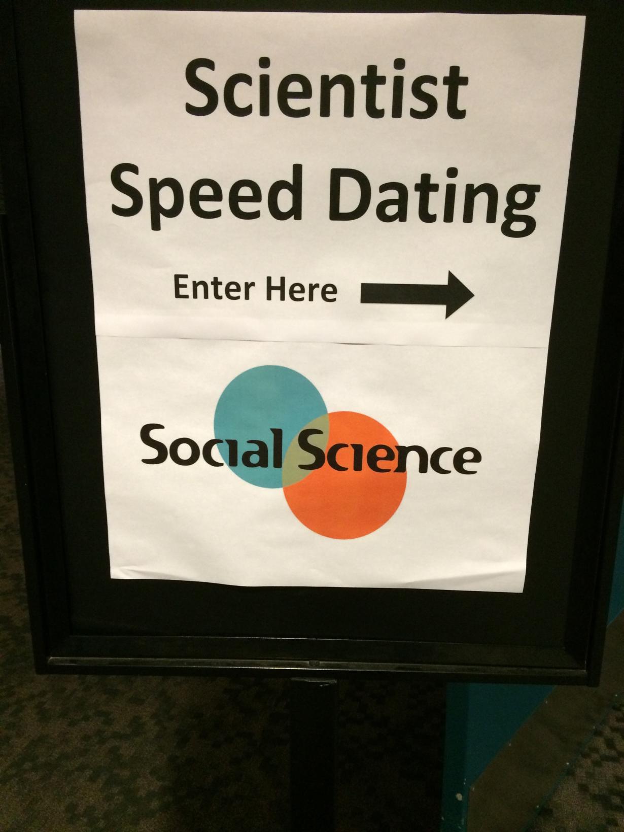 A white sign reading "Scientist Speed Dating, Enter Here"  