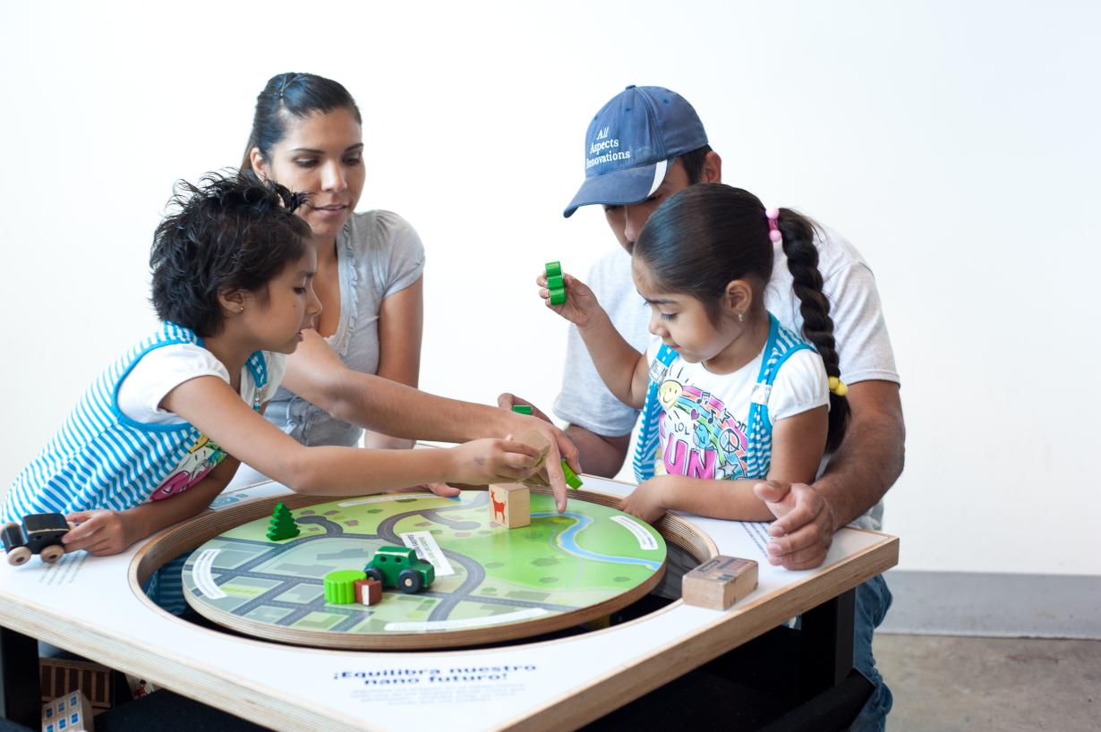 Family of four arrange objects that represent different nano subjects on a balance table