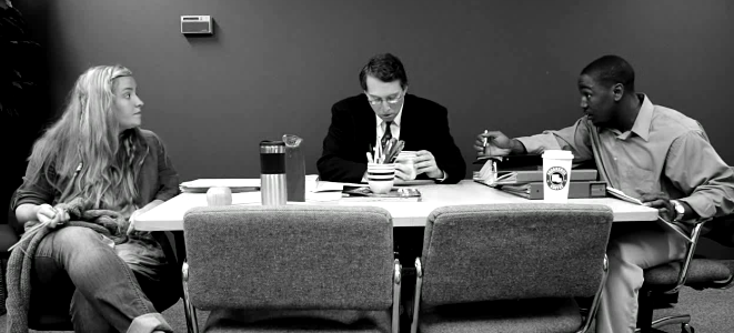 A black and white photo of three people sitting at a table having an intense discussion