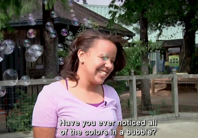 Lady in pink shirt stands in the path of a cluster of bubbles