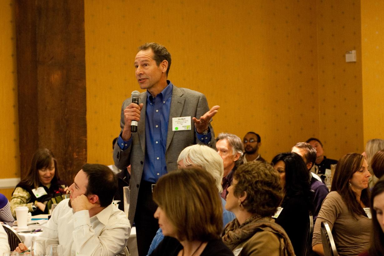 Man standing with microphone in a group forum discussing STEM topics societal implications
