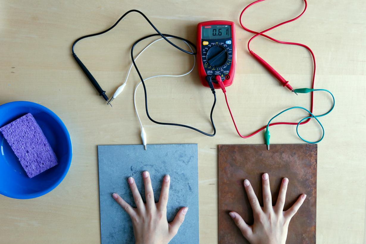 Participant's hands touching the steel and copper plates, connected to a multimeter