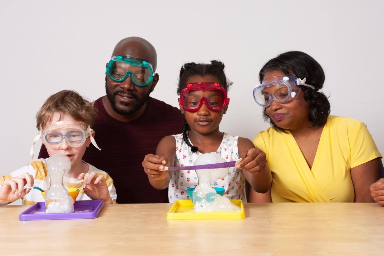 Two facilitators and two learners wearing goggles use colorful felt strips to layer bubbles upon each other