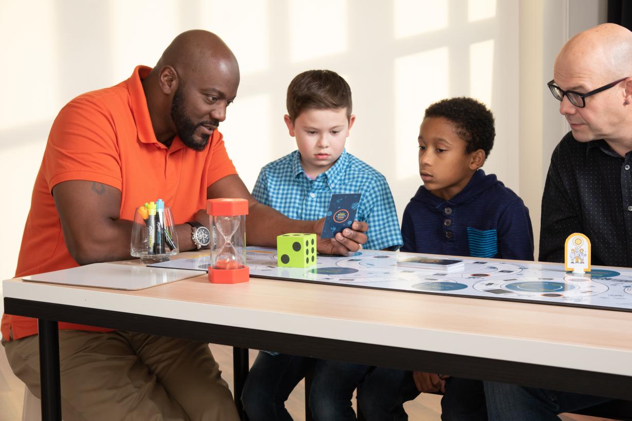 Family of four reads a game card for the Mission to Space board game