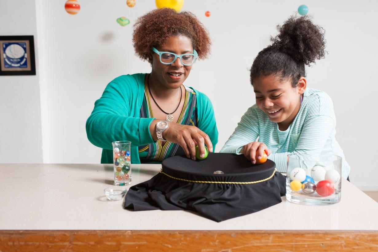 A learner and facilitator place a heavy ball in the middle of a fabric stretched well