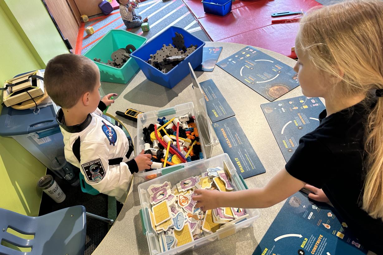 Design Build Test Space Weekend Activity with Boy Dressed as Astronaut and Girl Reaching for Building Pieces