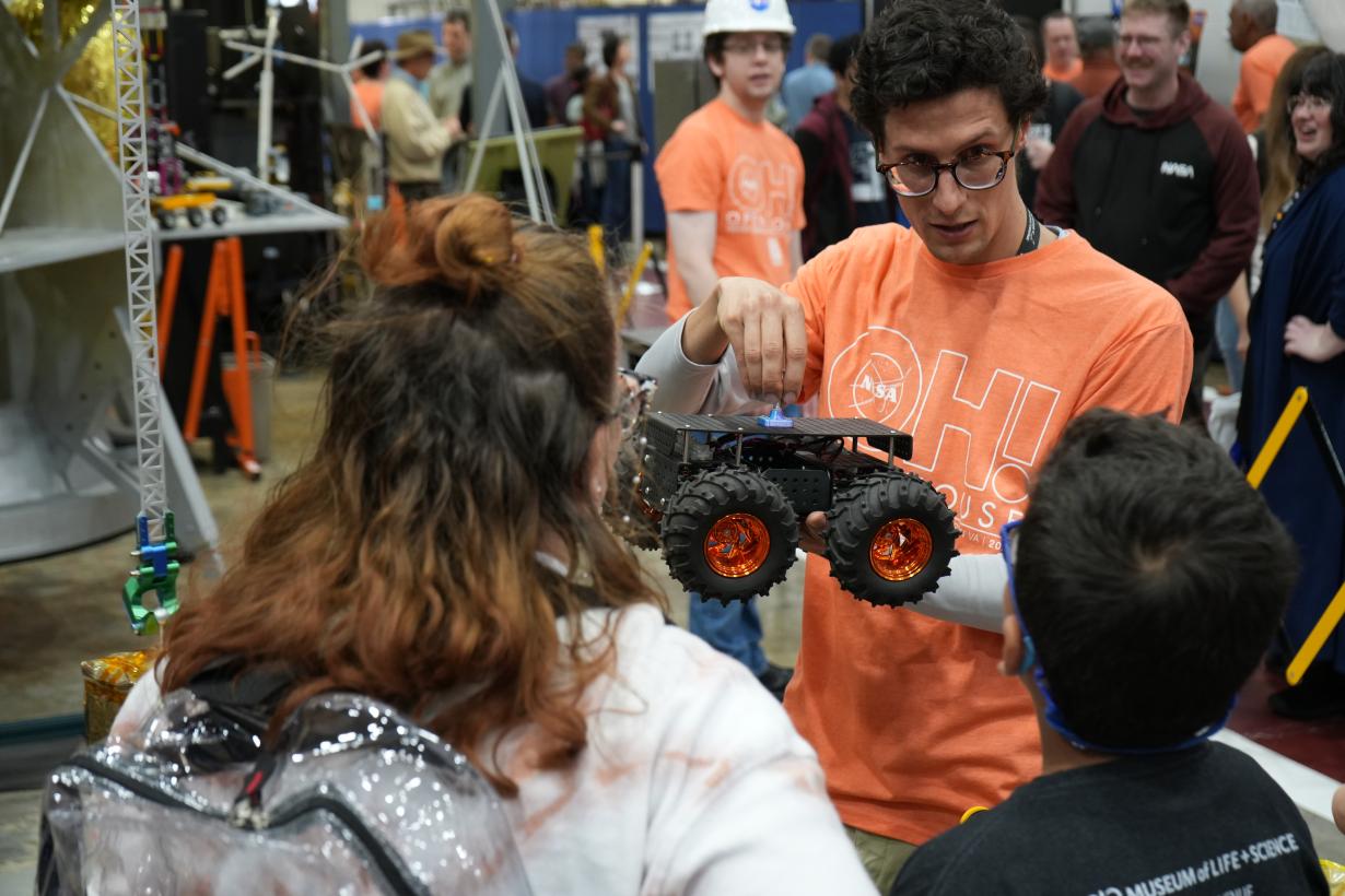 Educator Holds a Rover Model as Two Youth Listen and Learn More