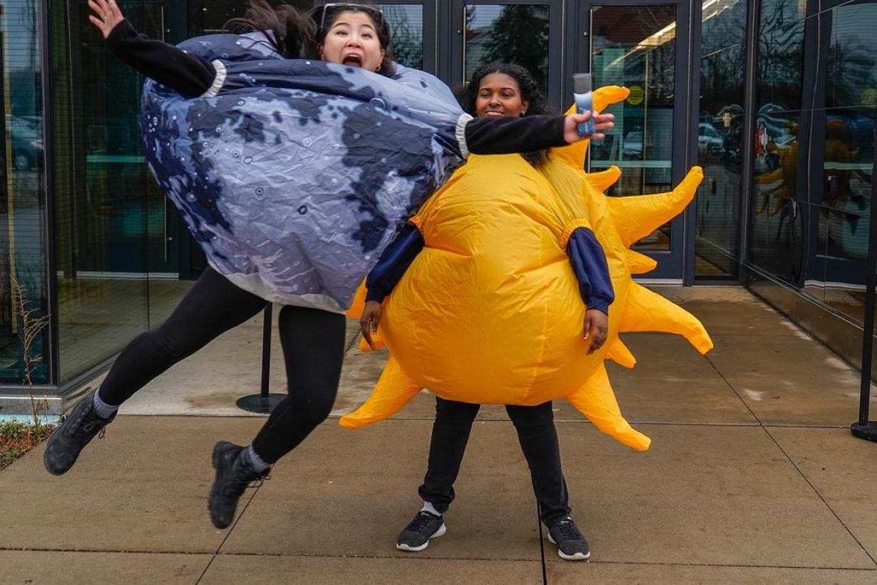 Two staff stand at The Bell Museum entrance and reenact the eclipse, one dressed as the Moon jumps in front to of the other dressed as the Sun to block it out.