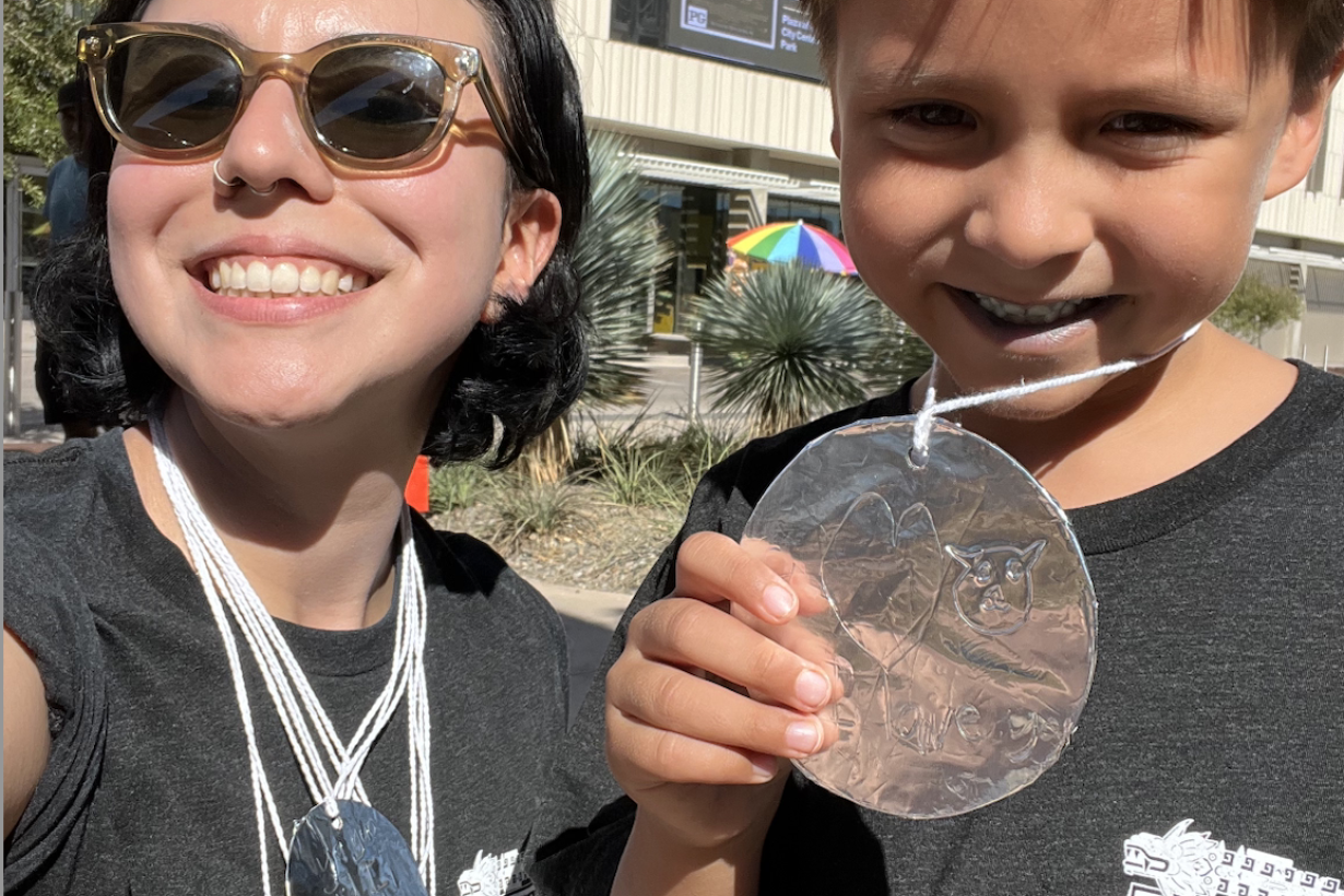 Woman and child pose smiling in the Sun, wearing black t-shirts and tin foil made medallions 