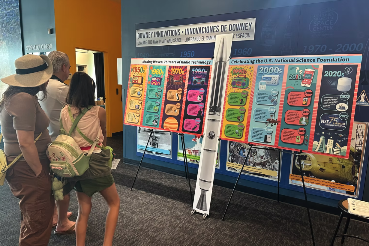 A family views a colorful, large-format radio technology timeline display at a science center exhibit. Ask ChatGPT
