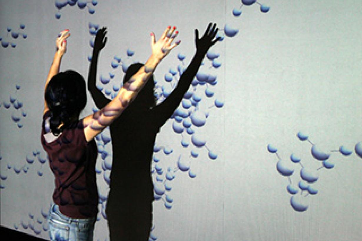 Young learner playing with a wall projection of molecules 