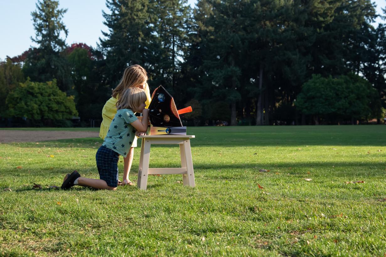 Two learners observe the Sun with a solarscope in a grassy field