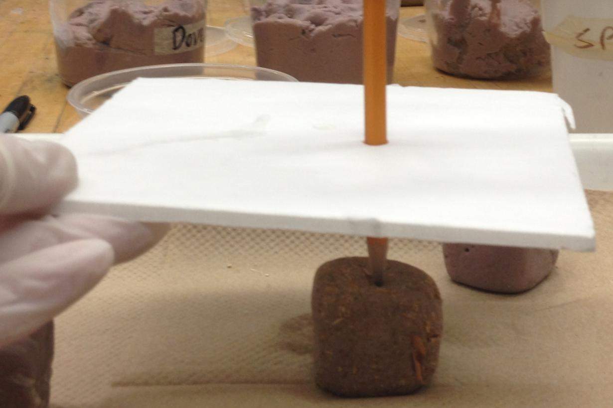 Brick design being tested by student featuring a pencil wedged in a Styrofoam board balancing a glass jar on a homemade brick