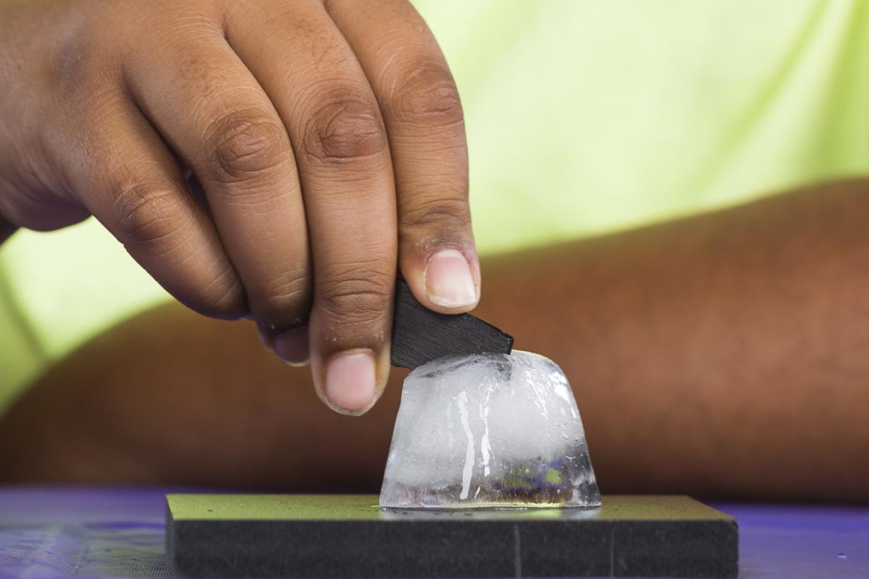 A person using thin slice of graphite to cut ice.