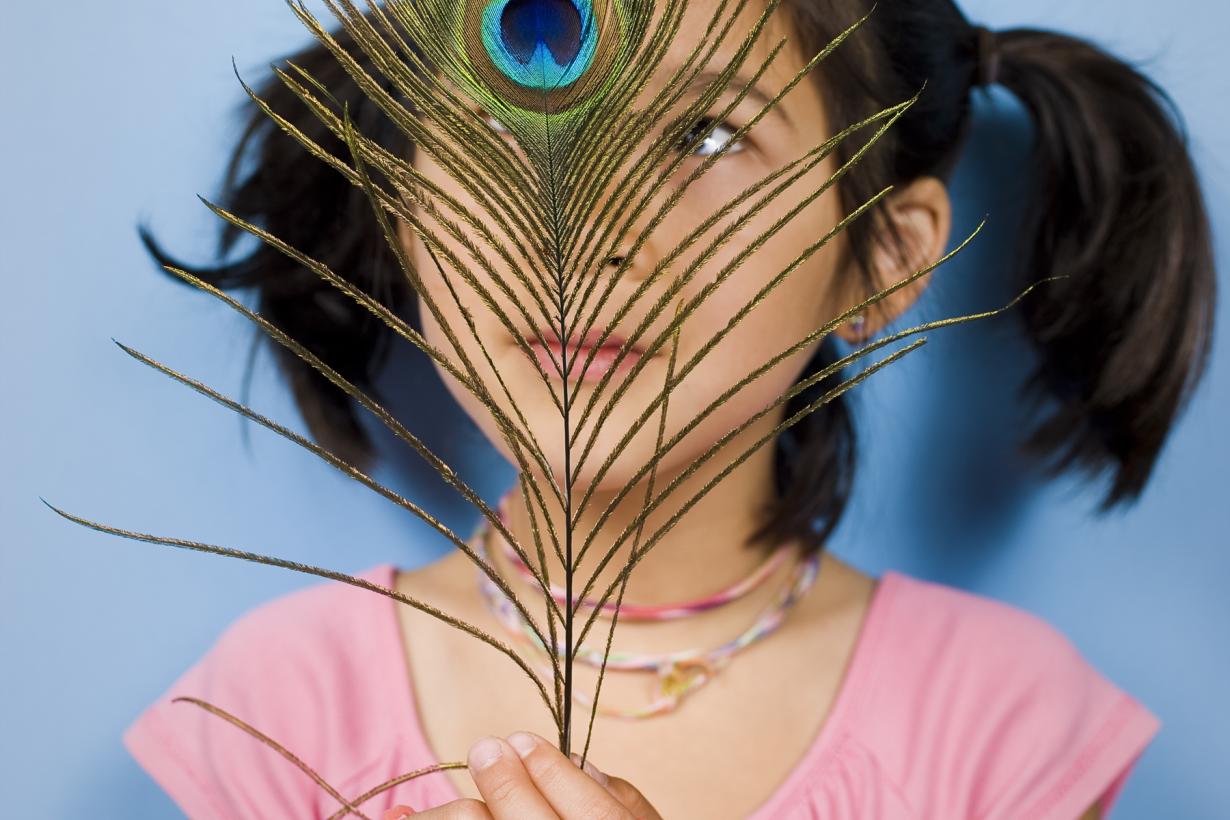 Girl in a pink shirt with staring at a peacock feather