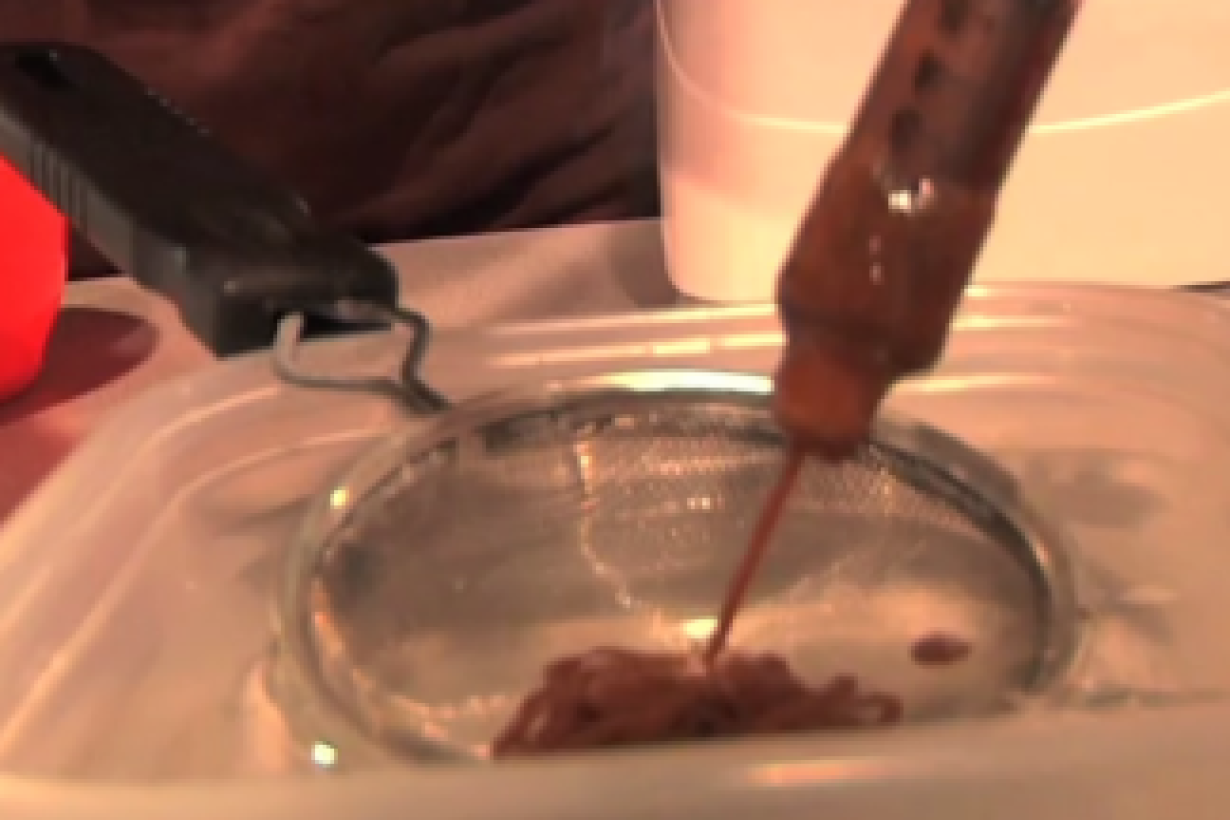 syringe of brownish gel ejecting into a small strainer over a bucket