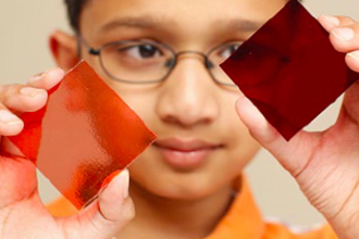 Child holding squares of red stained glass colored by nano gold