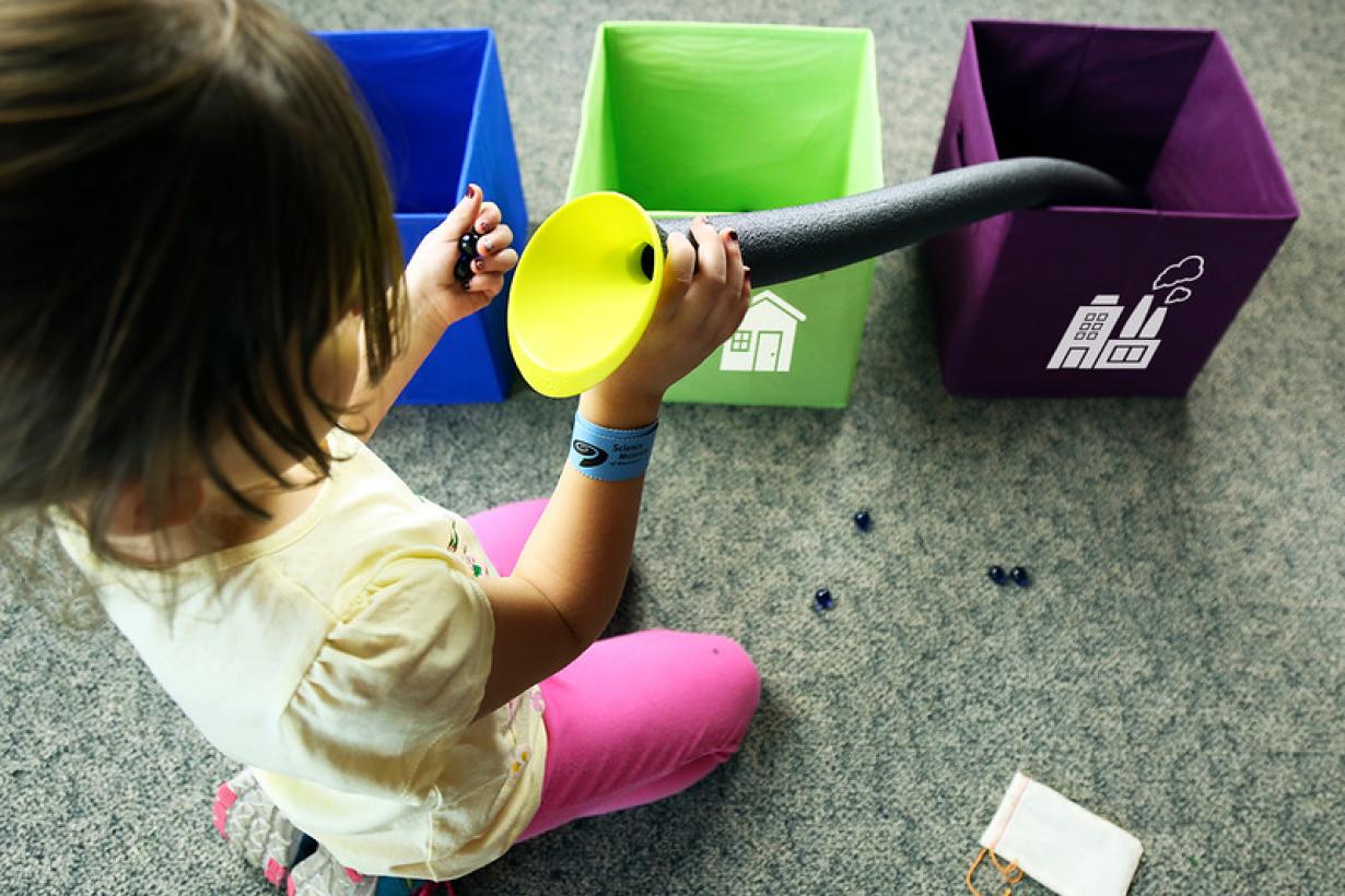 Young learner sorting colored marbles into three different colored boxes using a tube and funnel