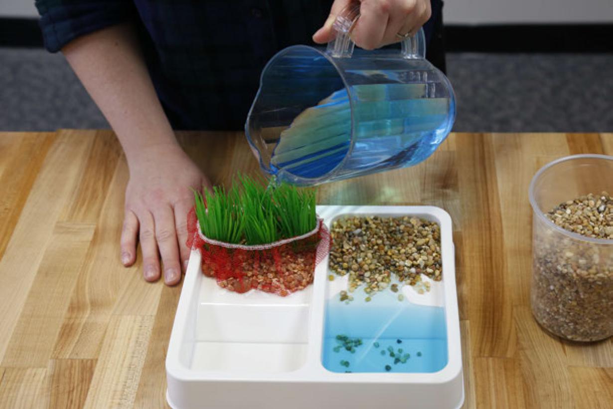 Photo of person pouring water on soil and sand to demonstrate erosion